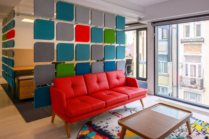 Fluffo Web als bunter Raumteiler in einer Lounge mit rotem Sofa