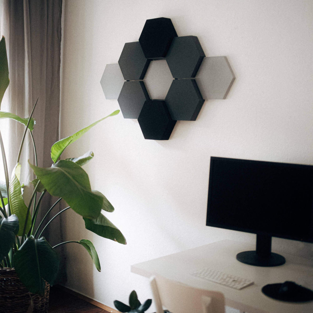 Schreibtisch mit Monitor, dahinter Velvet Hexa Light in Grautönen an der Wand